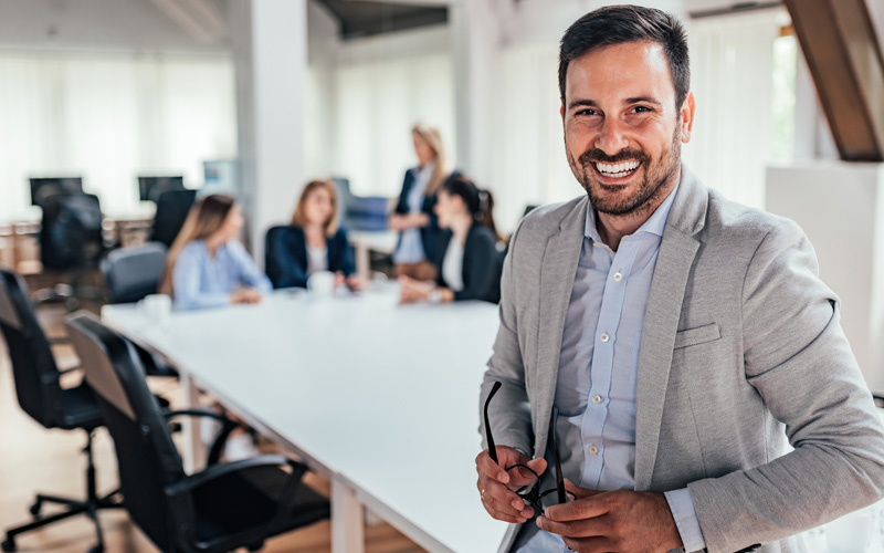 Lächelnder Mann im Besprechungsraum, Kollegen im Hintergrund