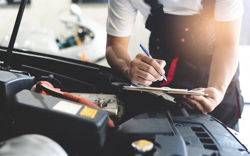 Werkstattmitarbeiter mit Klemmbrett über Motorhaube